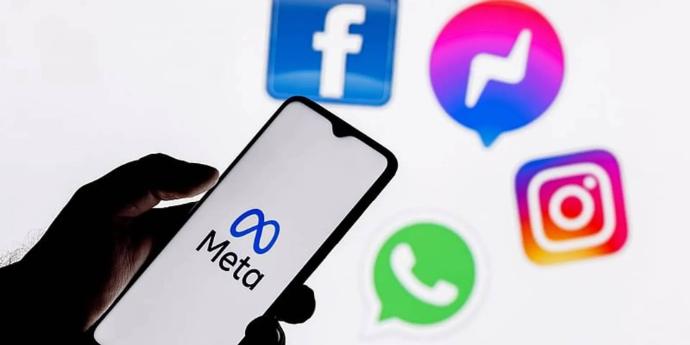 Hand holding smartphone with Meta logo, background showing WhatsApp, Facebook, and Instagram icons